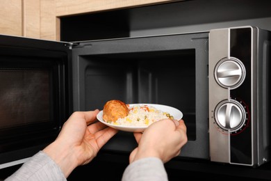 Photo of Man putting plate with lunch into microwave in kitchen, closeup