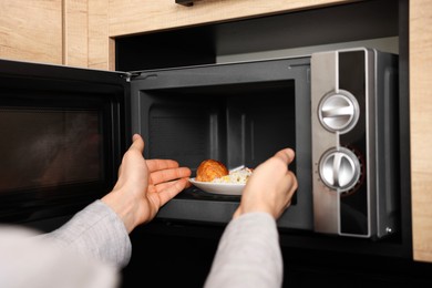 Man putting plate with lunch into microwave in kitchen, closeup