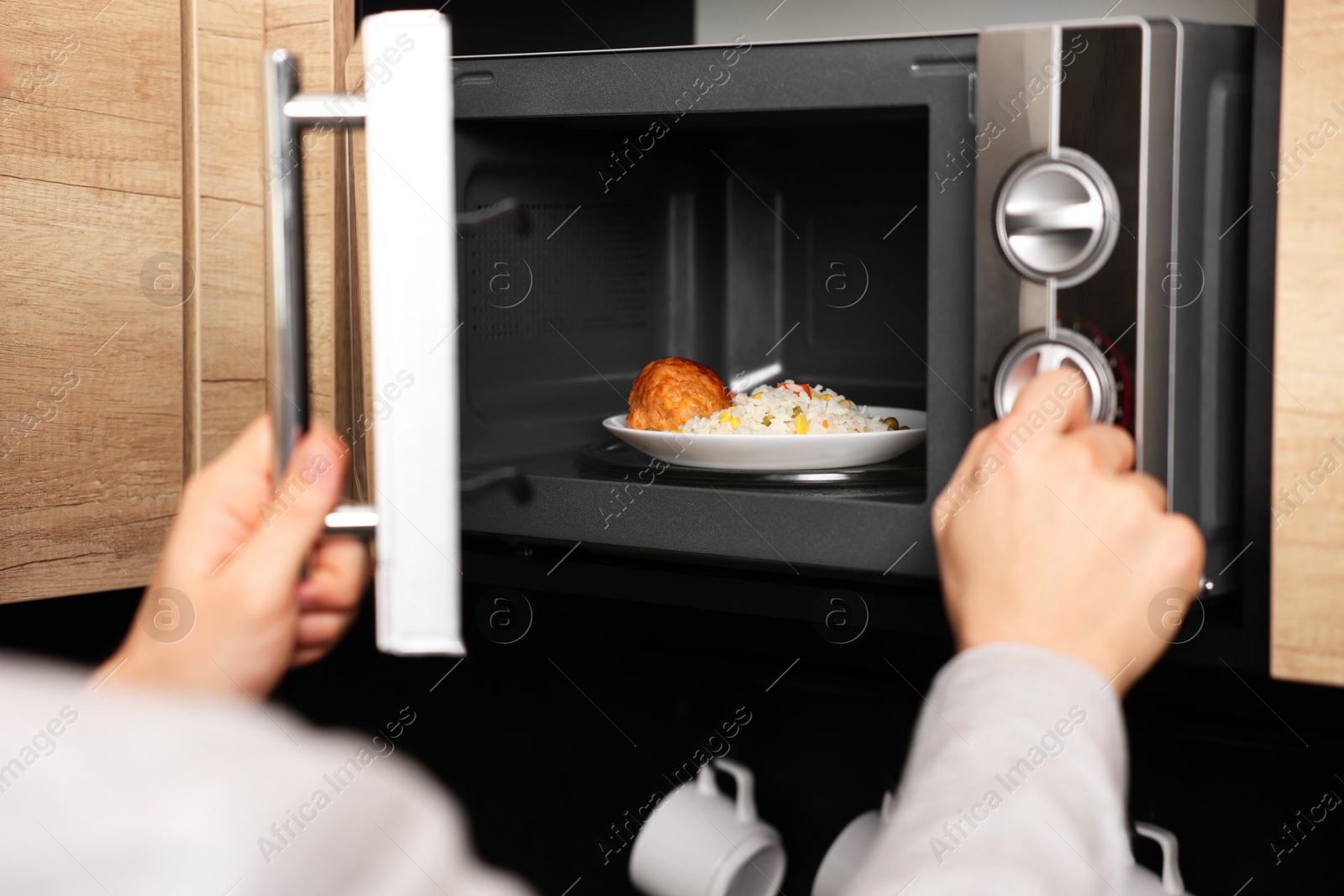 Photo of Man putting plate with lunch into microwave in kitchen, closeup