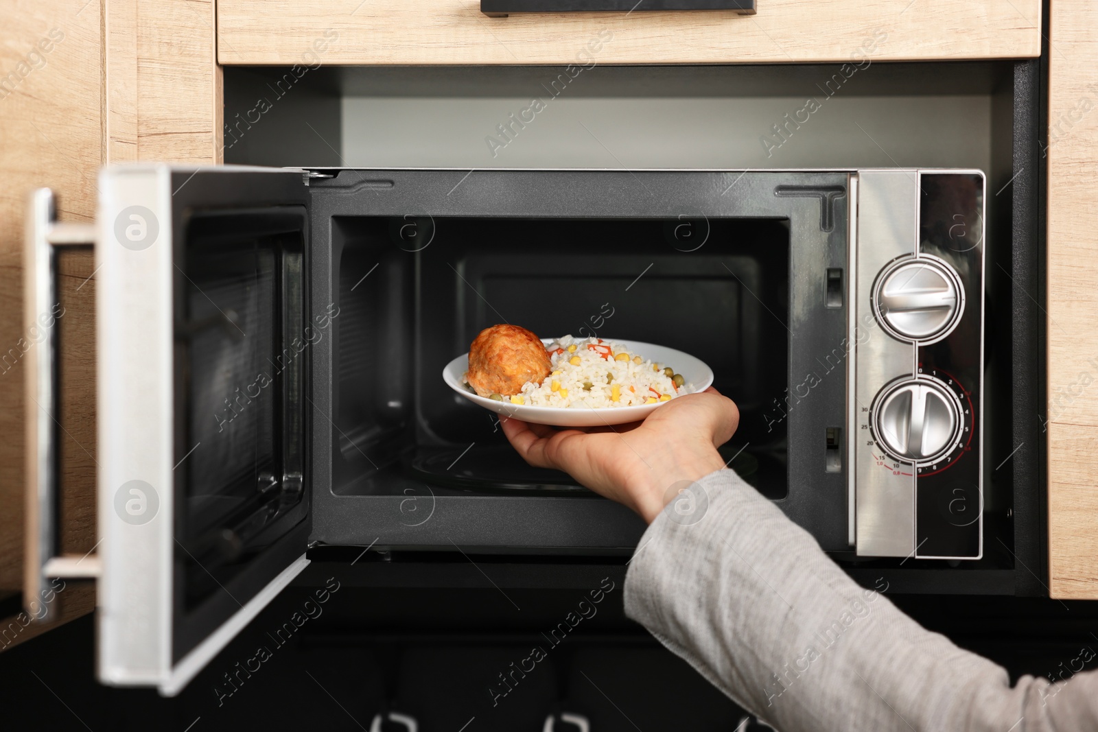 Photo of Man putting plate with lunch into microwave in kitchen, closeup