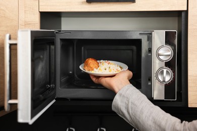 Man putting plate with lunch into microwave in kitchen, closeup