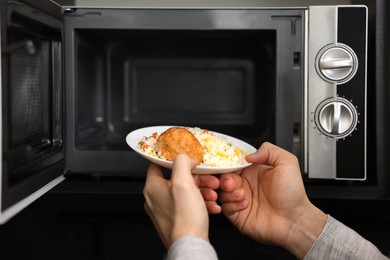 Man putting plate with lunch into microwave in kitchen, closeup