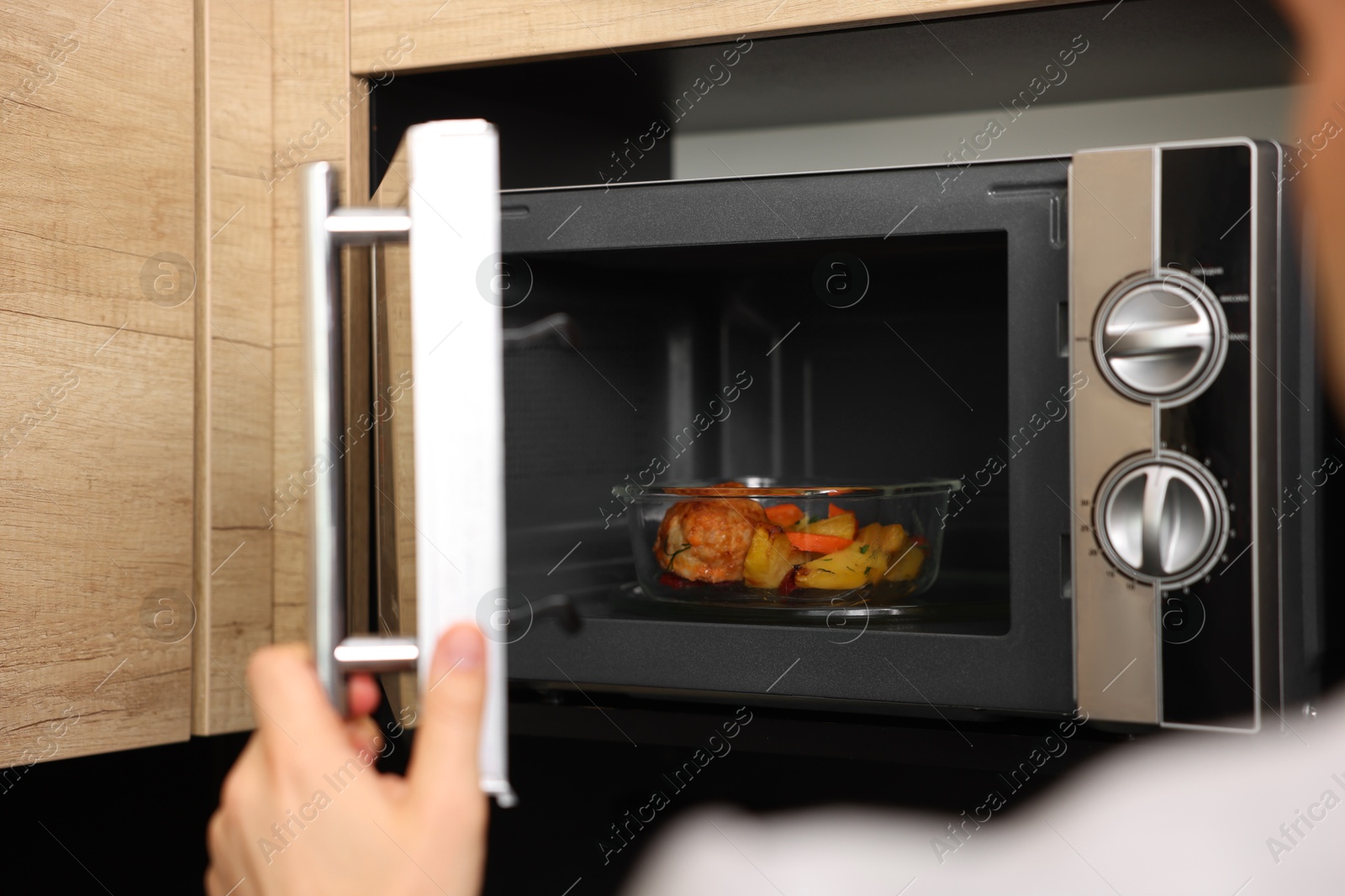 Photo of Man putting container with lunch into microwave in kitchen, closeup