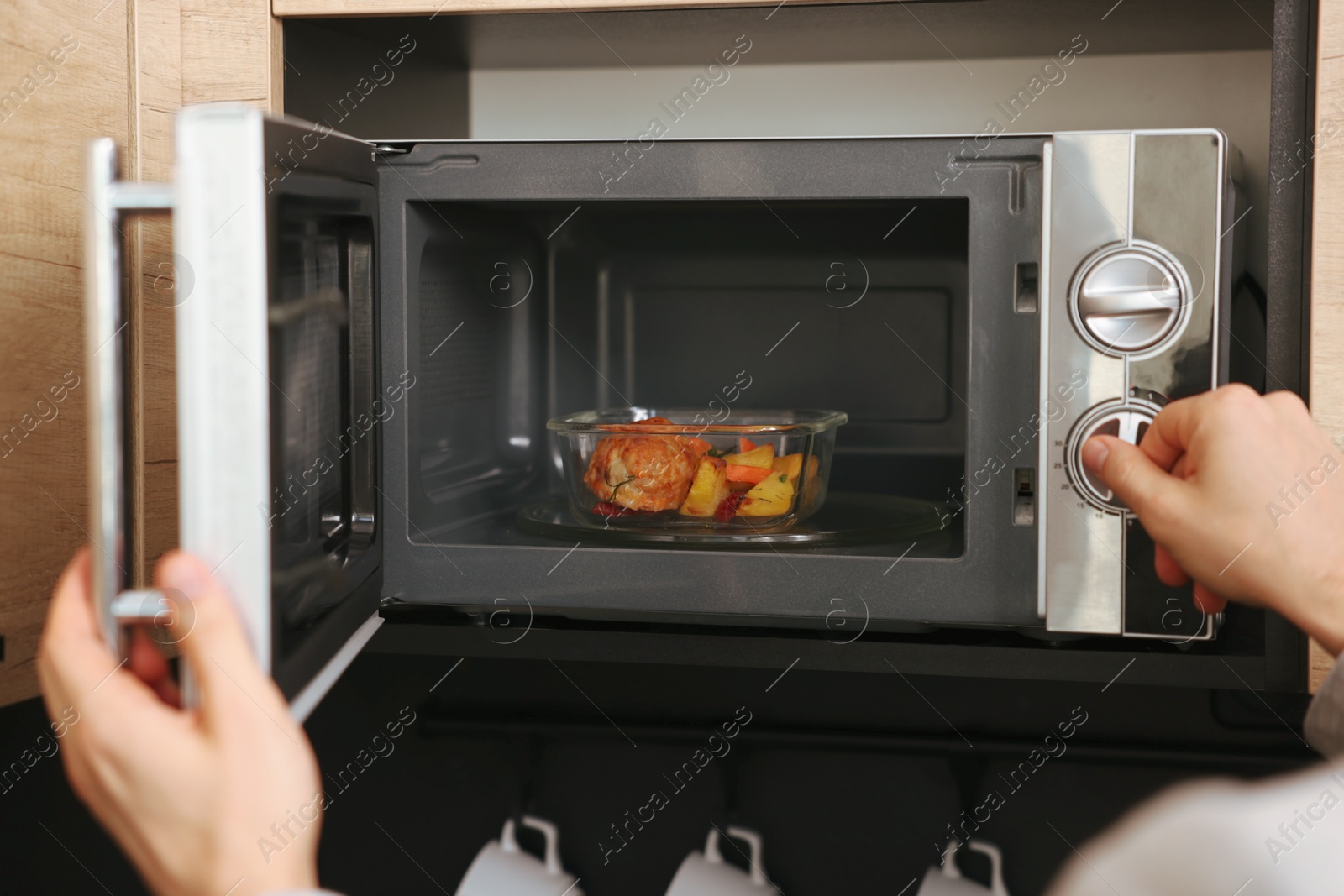 Photo of Man putting container with lunch into microwave in kitchen, closeup