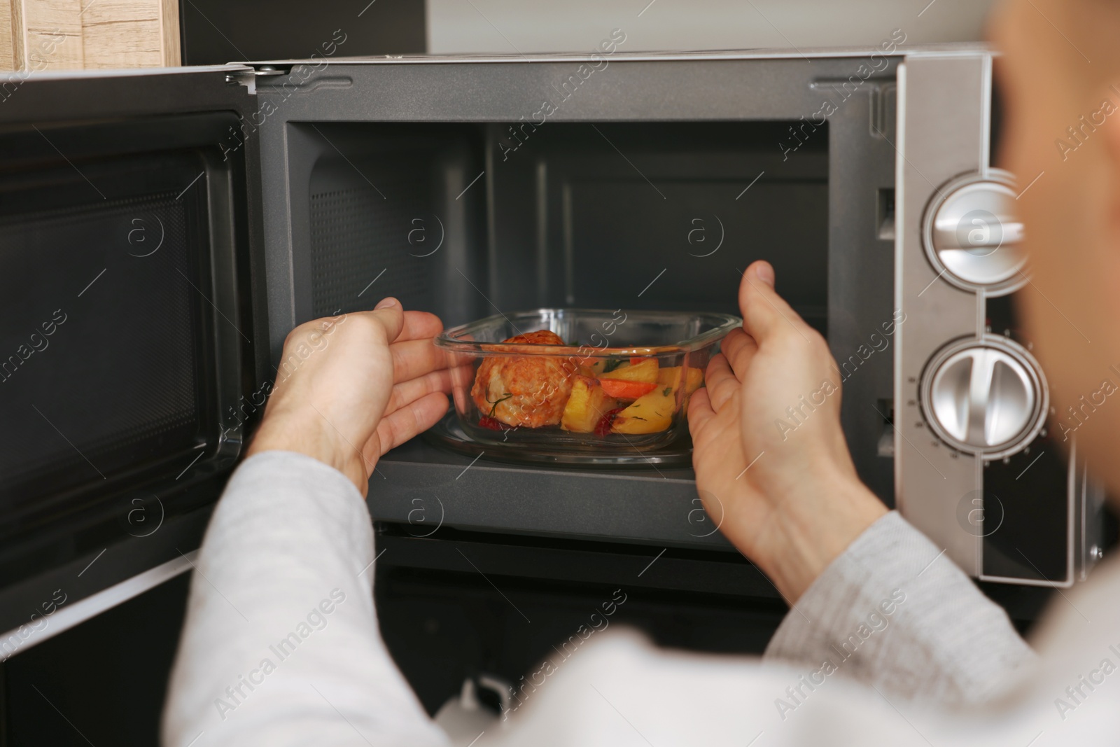 Photo of Man putting container with lunch into microwave in kitchen, closeup