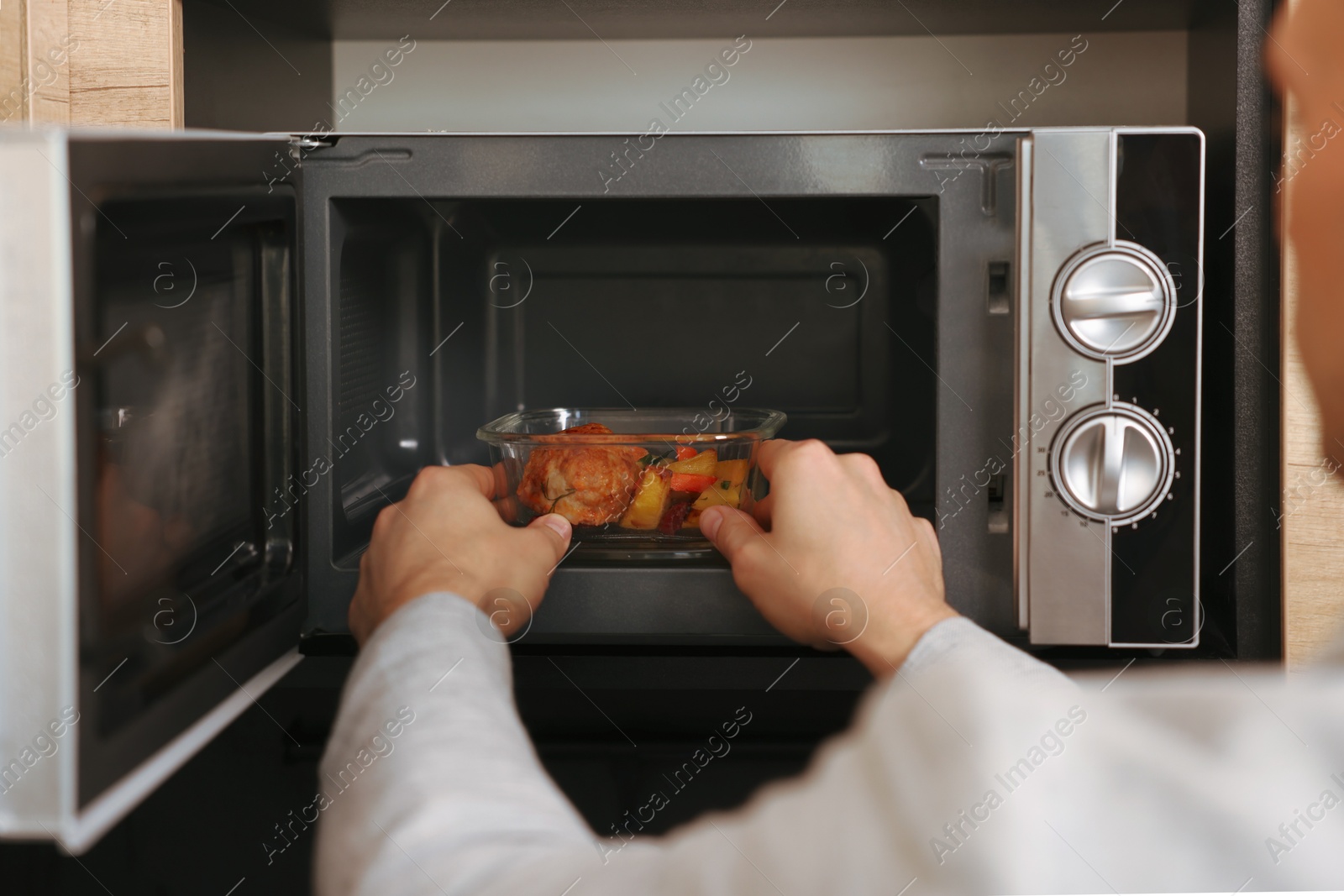 Photo of Man putting container with lunch into microwave in kitchen, closeup