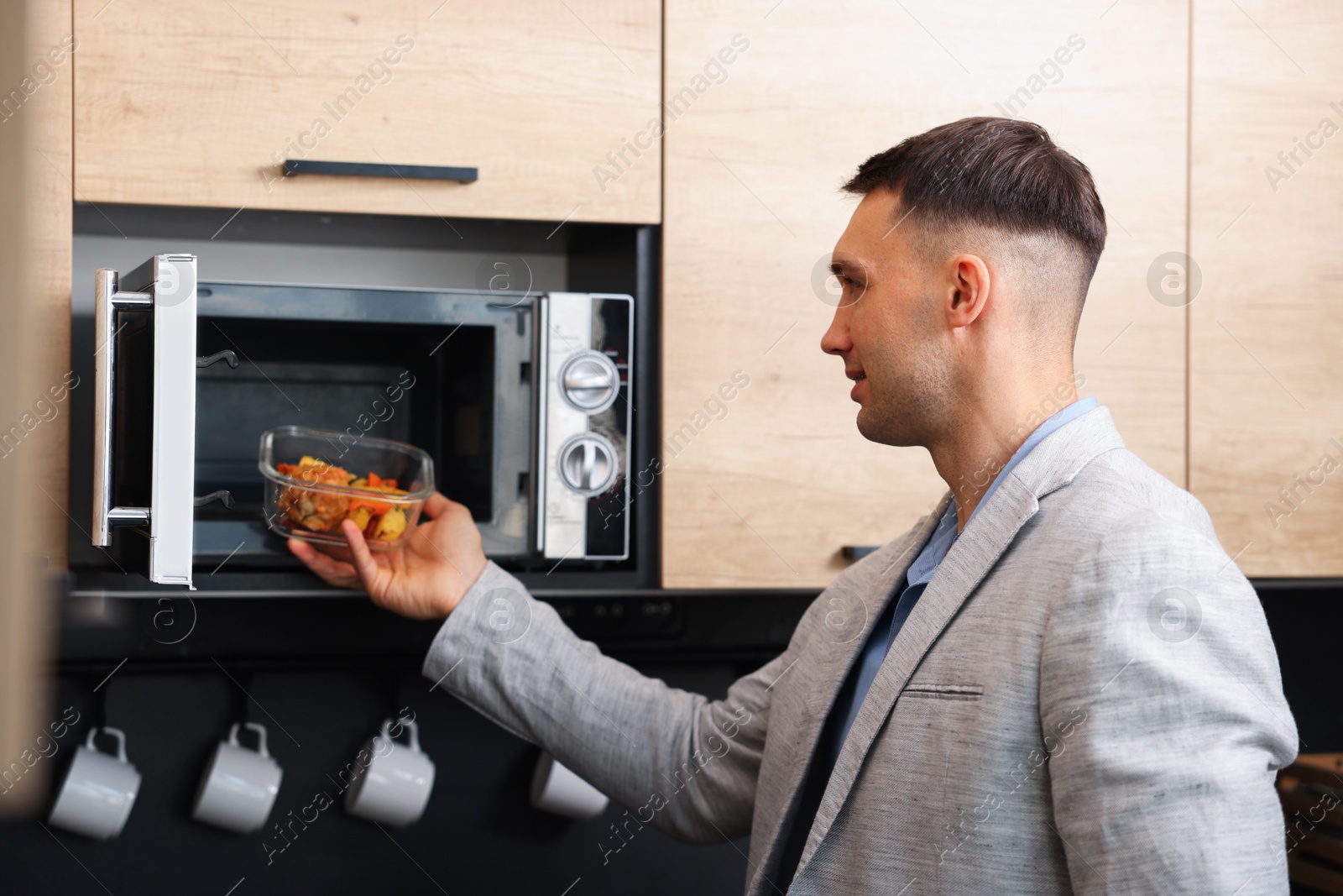 Photo of Man putting container with lunch into microwave in kitchen