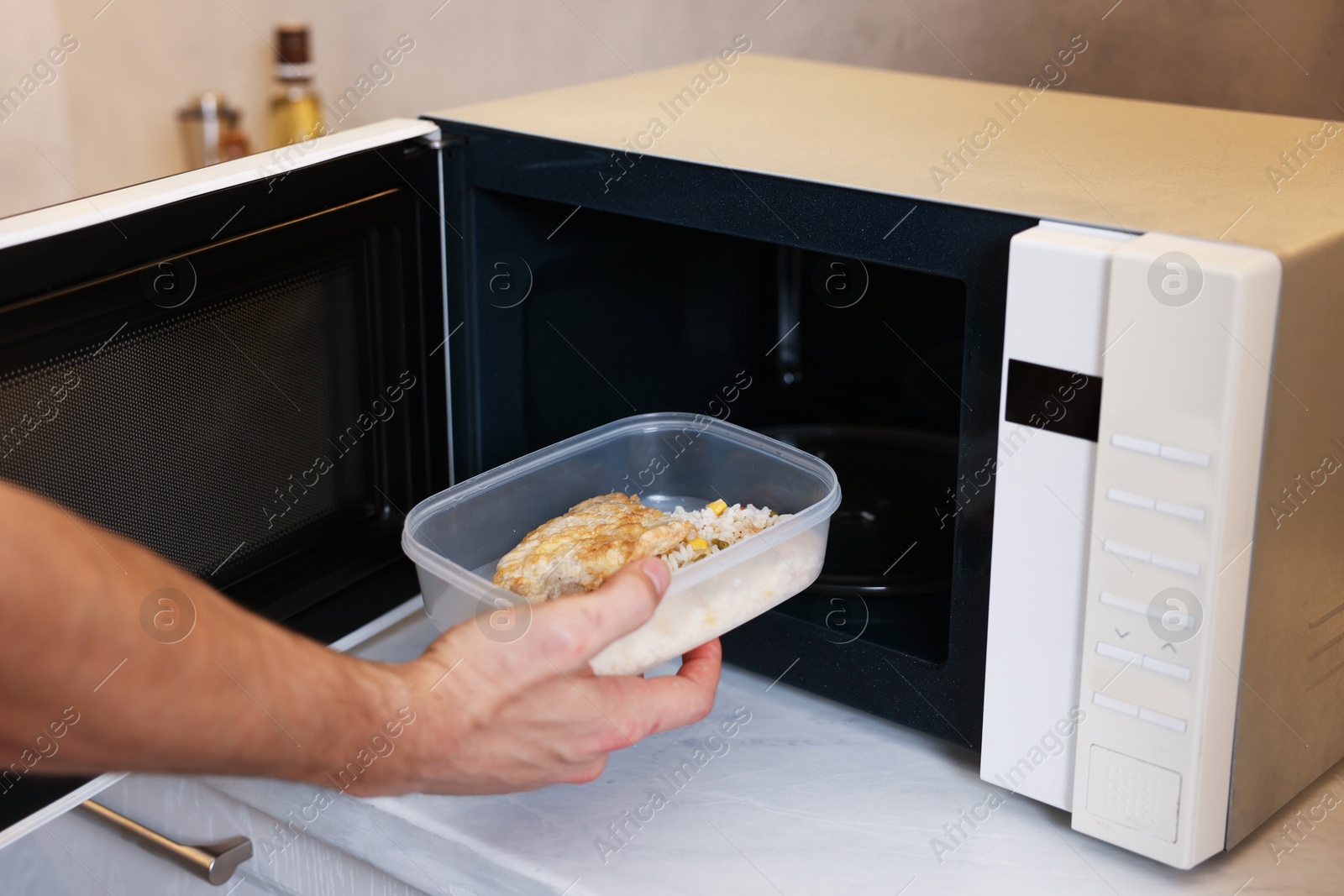 Photo of Man putting container with lunch into microwave in kitchen, closeup