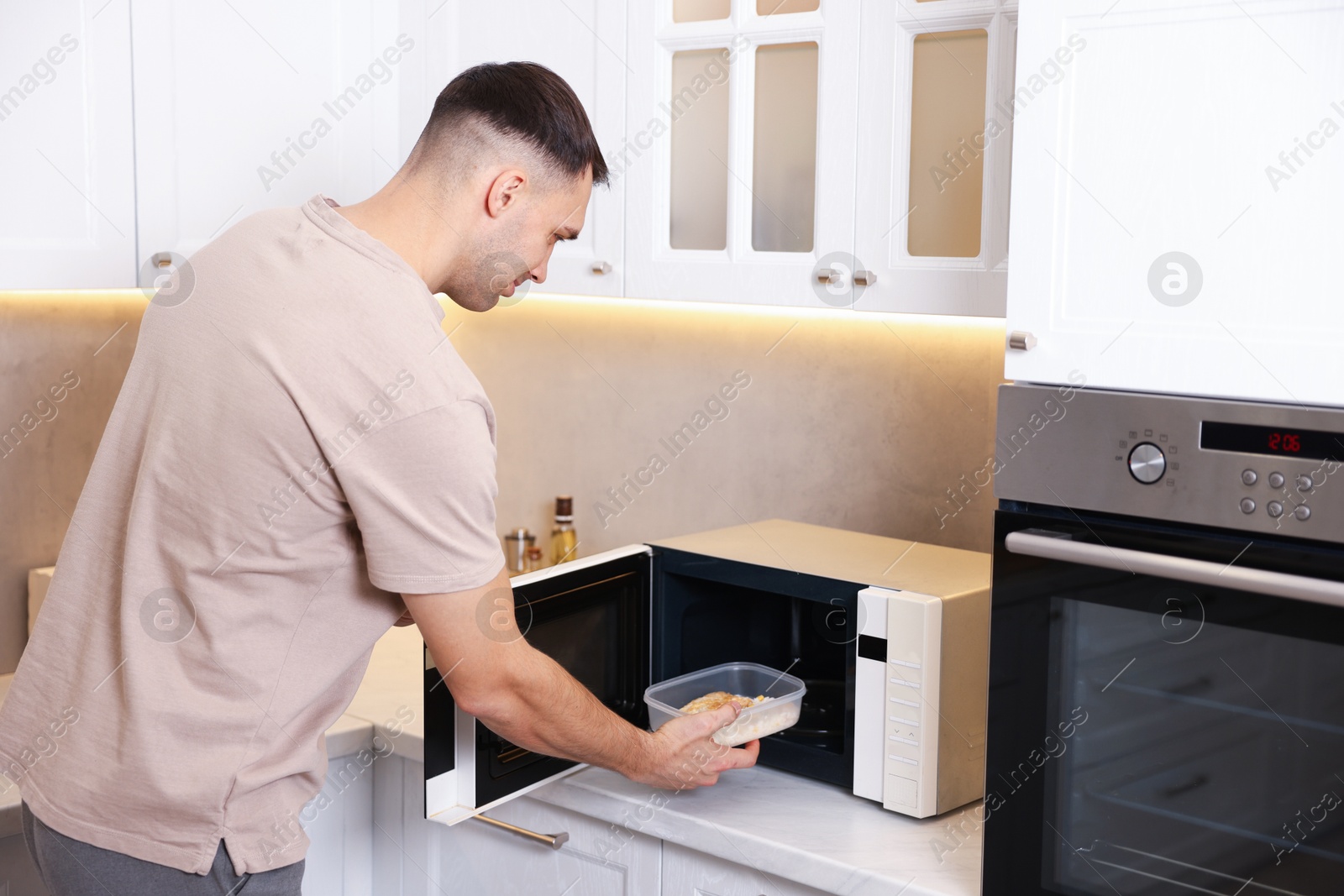 Photo of Man putting container with lunch into microwave in kitchen