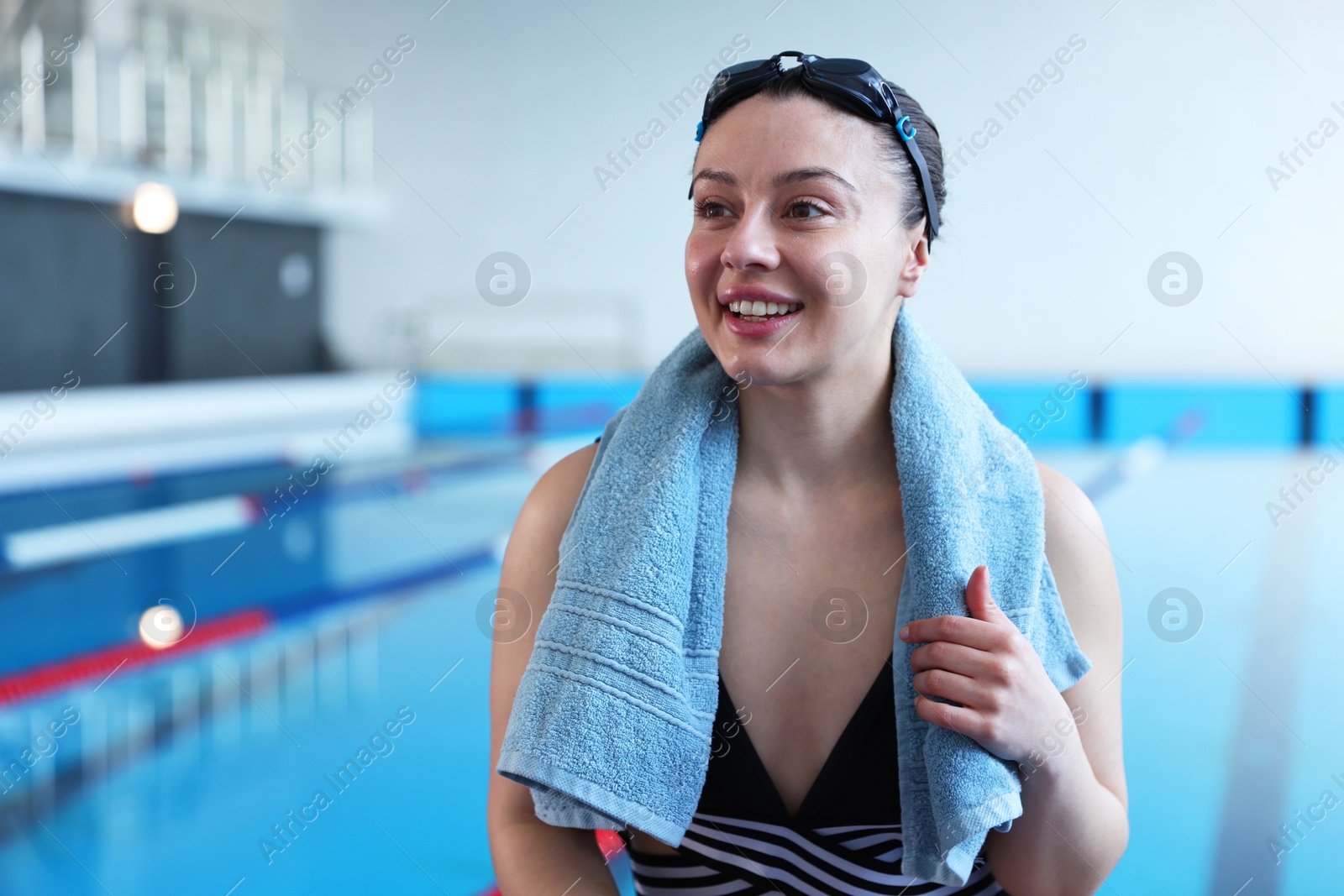 Photo of Happy woman with goggles, swimsuit and towel near swimming pool indoors