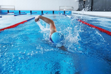 Young man in cap and goggles swimming in pool indoors