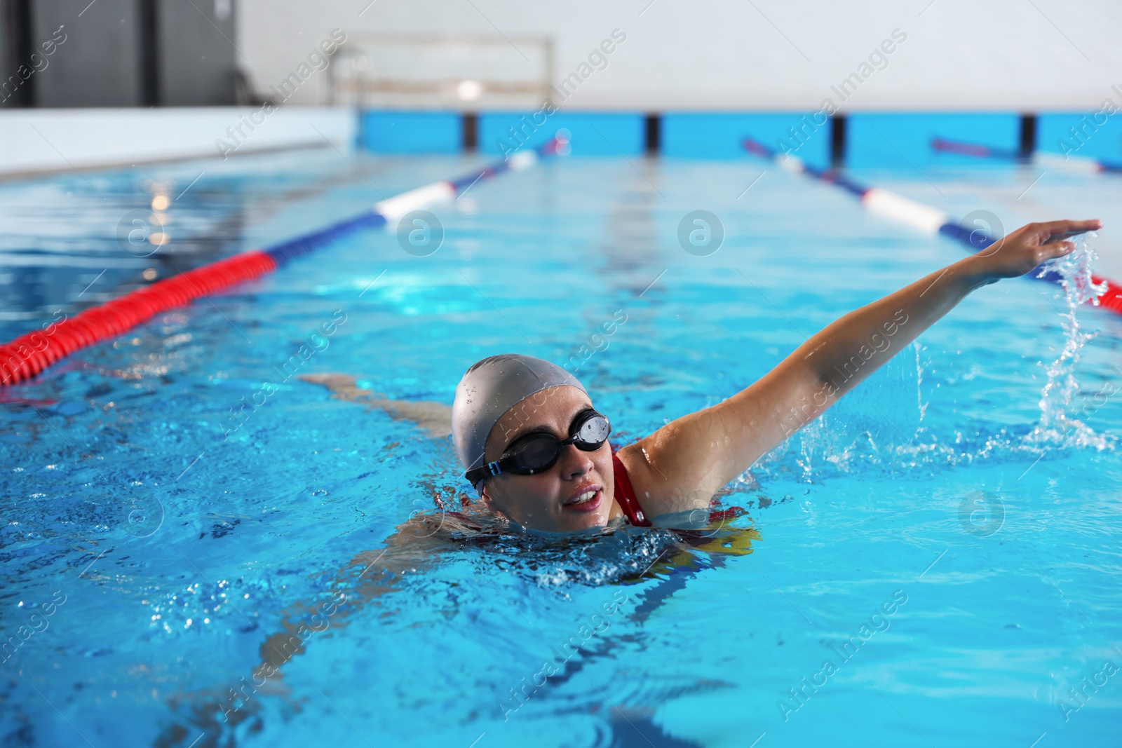 Photo of Woman in cap, goggles and swimsuit swimming in pool indoors