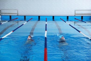 Young man and woman swimming in pool indoors