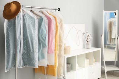 Photo of Garment covers with clothes and hat on rack near grey wall indoors