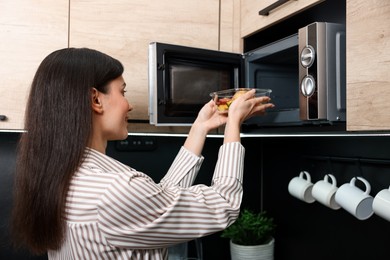 Photo of Woman putting container with lunch into microwave indoors