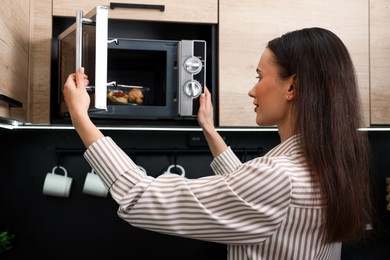 Photo of Woman putting container with lunch into microwave indoors