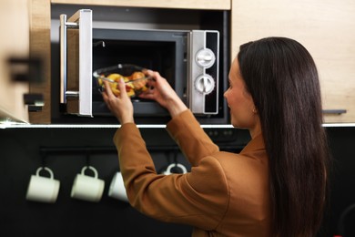 Woman putting container with lunch into microwave indoors