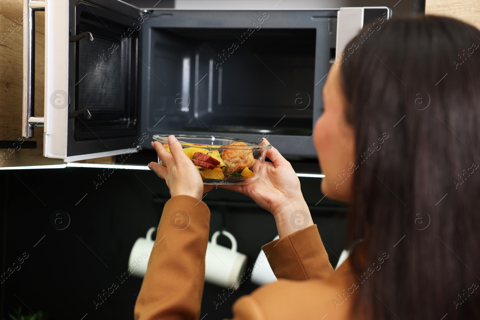 Photo of Woman putting container with lunch into microwave indoors