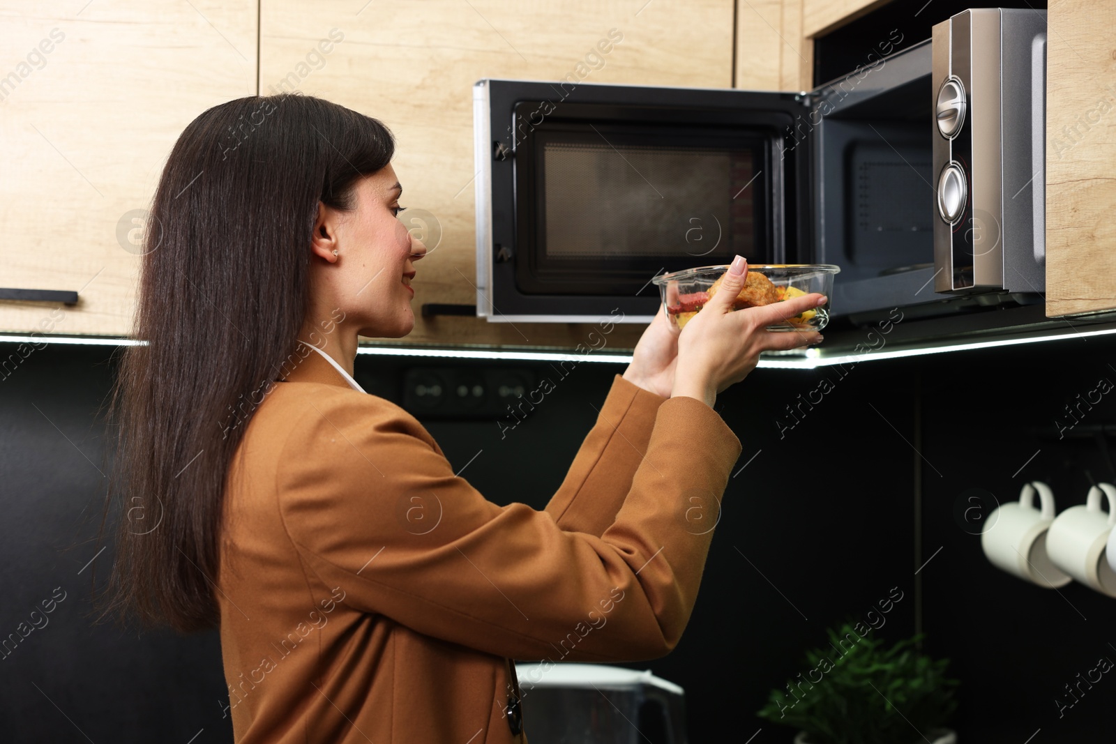 Photo of Woman putting container with lunch into microwave indoors