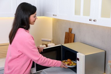 Woman putting plate with lunch into microwave indoors