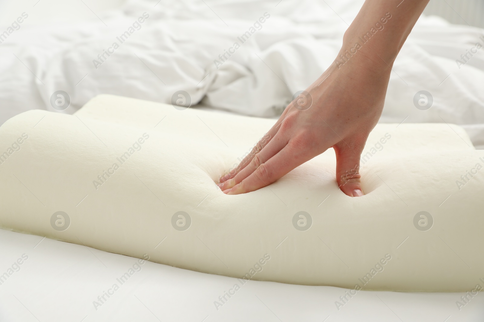 Photo of Woman touching orthopedic memory foam pillow on bed, closeup. Space for text