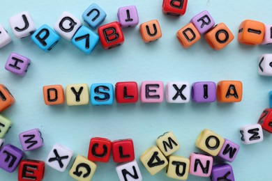 Colorful beads with word Dyslexia on light blue background, flat lay