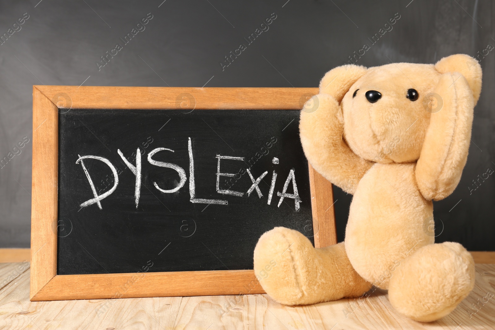 Photo of Teddy bear and small blackboard with word Dyslexia on wooden table