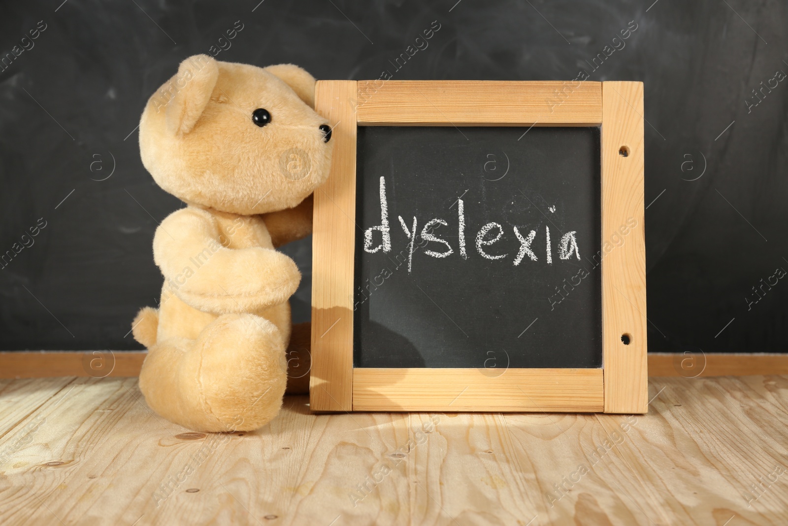 Photo of Teddy bear and small blackboard with word Dyslexia on wooden table