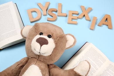 Photo of Word Dyslexia made of wooden letters, teddy bear and books on light blue background, above view