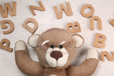 Photo of Dyslexia concept. Teddy bear with glasses and letters on light wooden table, flat lay