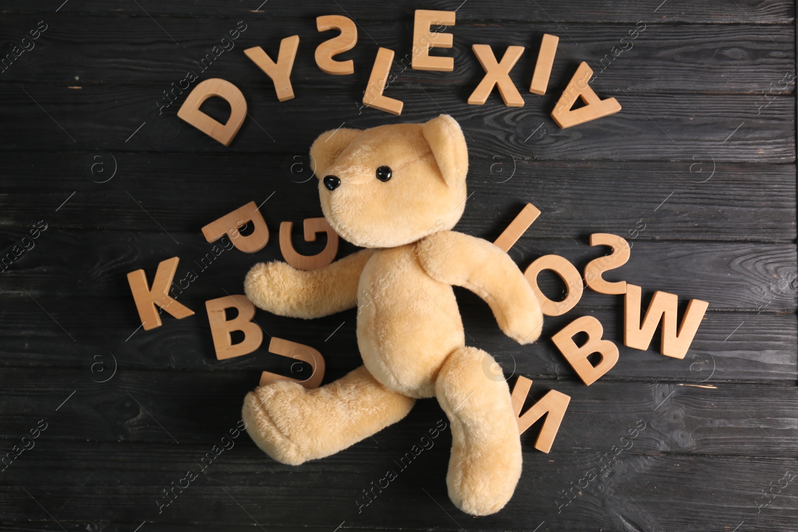 Photo of Word Dyslexia made of letters and teddy bear on dark wooden table, flat lay