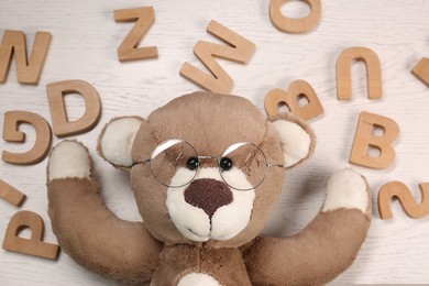 Photo of Dyslexia concept. Teddy bear with glasses and letters on light wooden table, flat lay