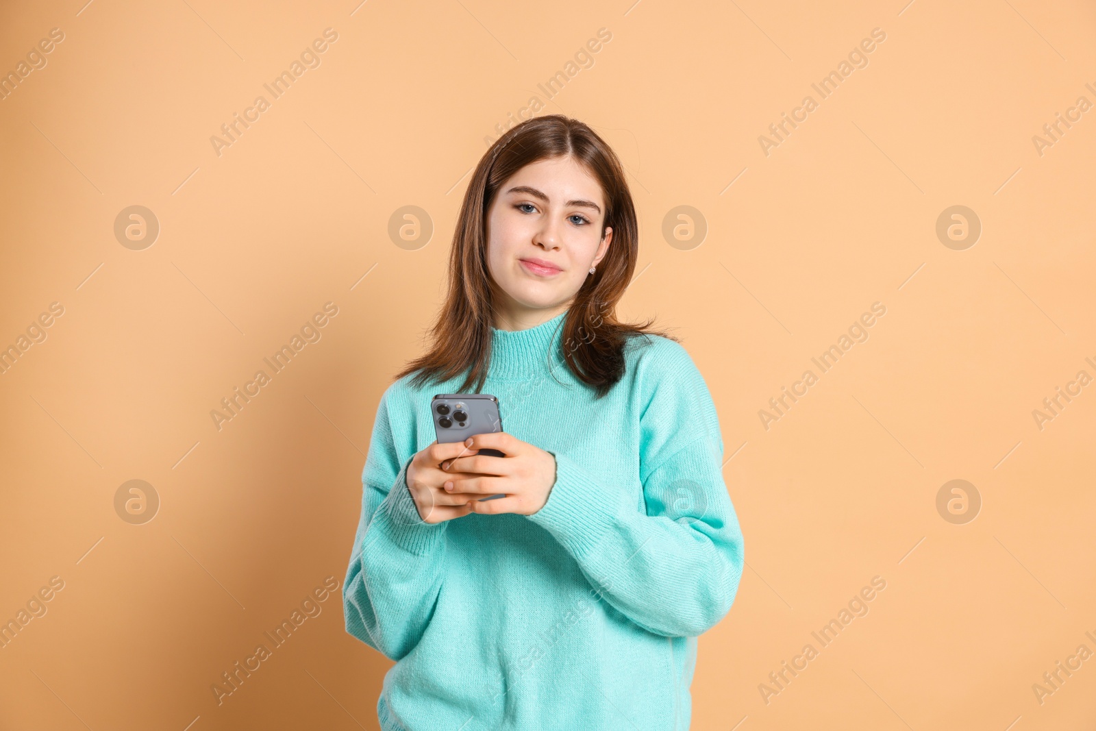 Photo of Portrait of beautiful teenage girl with smartphone on beige background