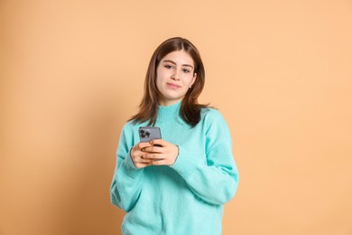 Portrait of beautiful teenage girl with smartphone on beige background