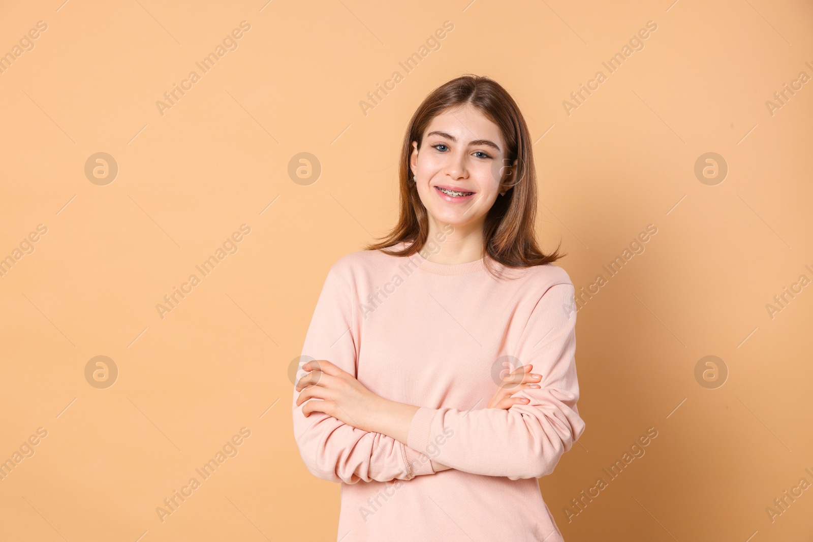 Photo of Portrait of beautiful teenage girl with crossed arms on beige background. Space for text