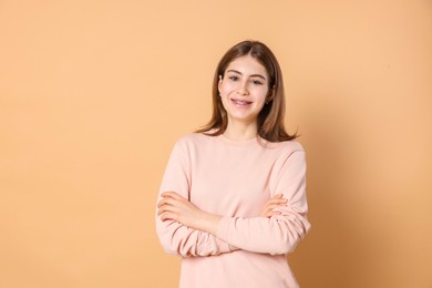 Portrait of beautiful teenage girl with crossed arms on beige background. Space for text