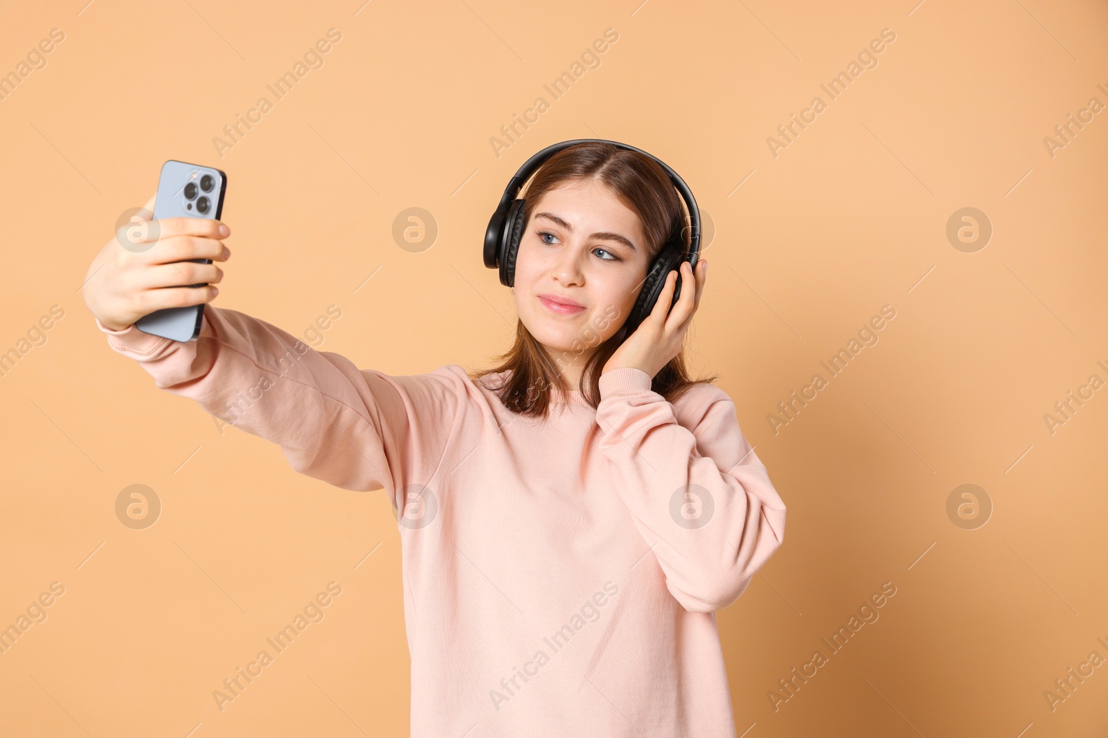 Photo of Portrait of teenage girl in headphones taking selfie on beige background