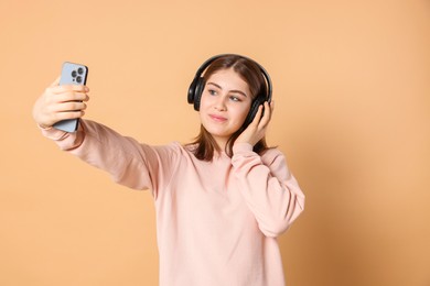 Portrait of teenage girl in headphones taking selfie on beige background