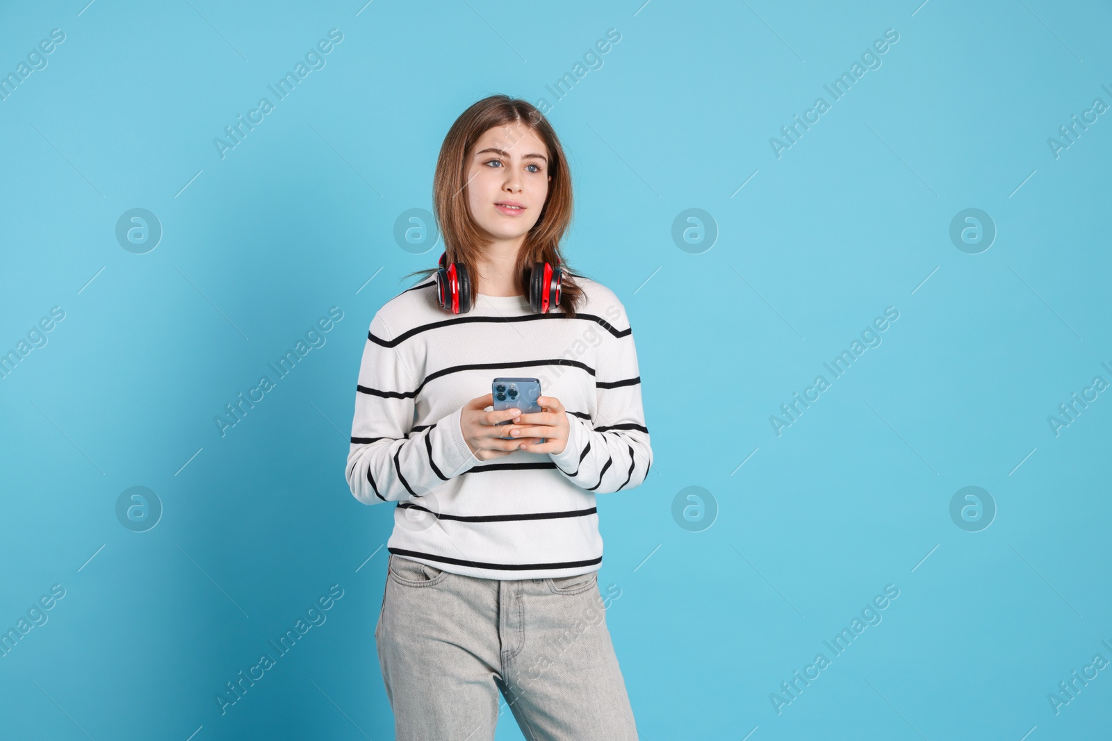 Photo of Portrait of teenage girl with headphones and smartphone on light blue background. Space for text