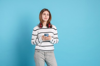 Portrait of teenage girl with headphones and smartphone on light blue background. Space for text