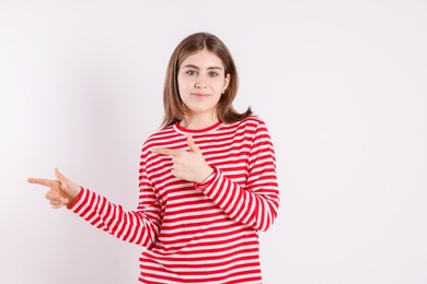 Portrait of teenage girl pointing at something on light background