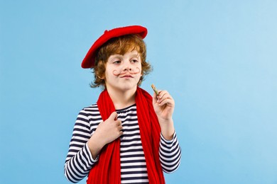 Photo of Cute boy in mime costume with brush on light blue background. Surprise party