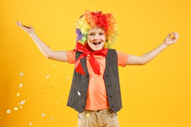 Photo of Happy little boy dressed like clown and flying confetti on orange background. Surprise party