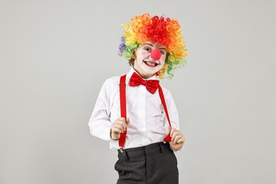 Photo of Happy little boy in clown wig and red nose on grey background. Surprise party