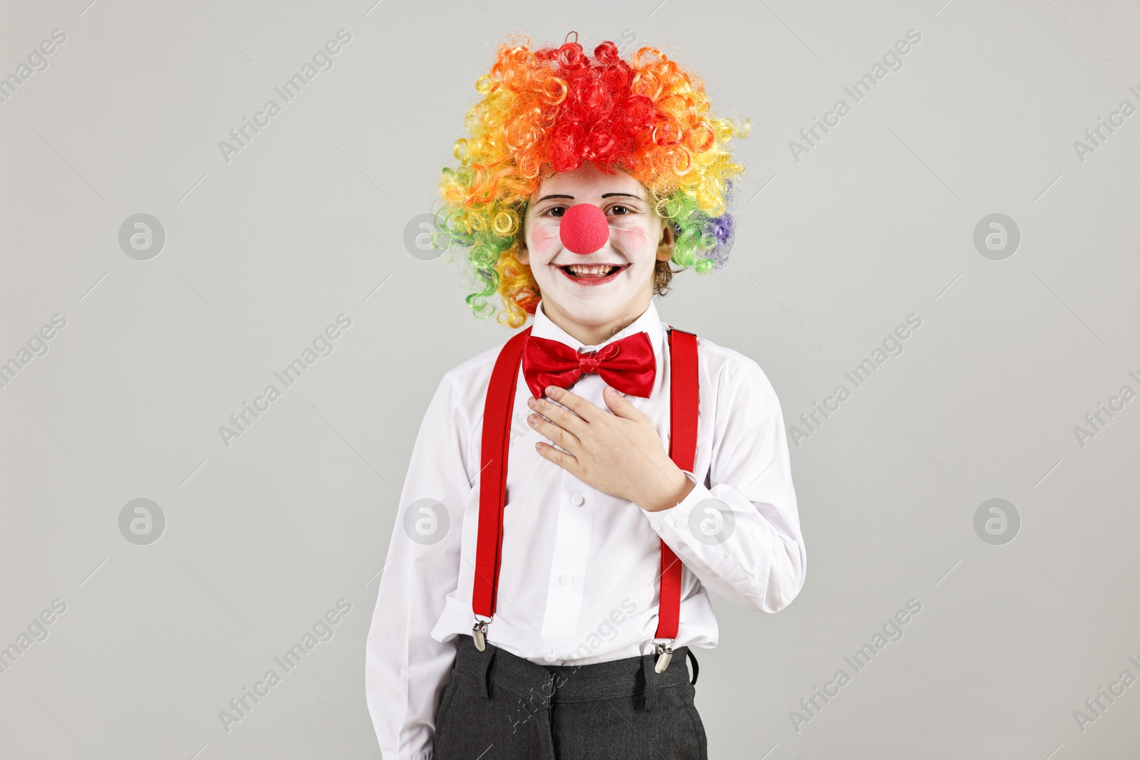 Photo of Happy little boy in clown wig and red nose on grey background. Surprise party