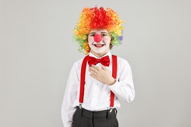 Happy little boy in clown wig and red nose on grey background. Surprise party