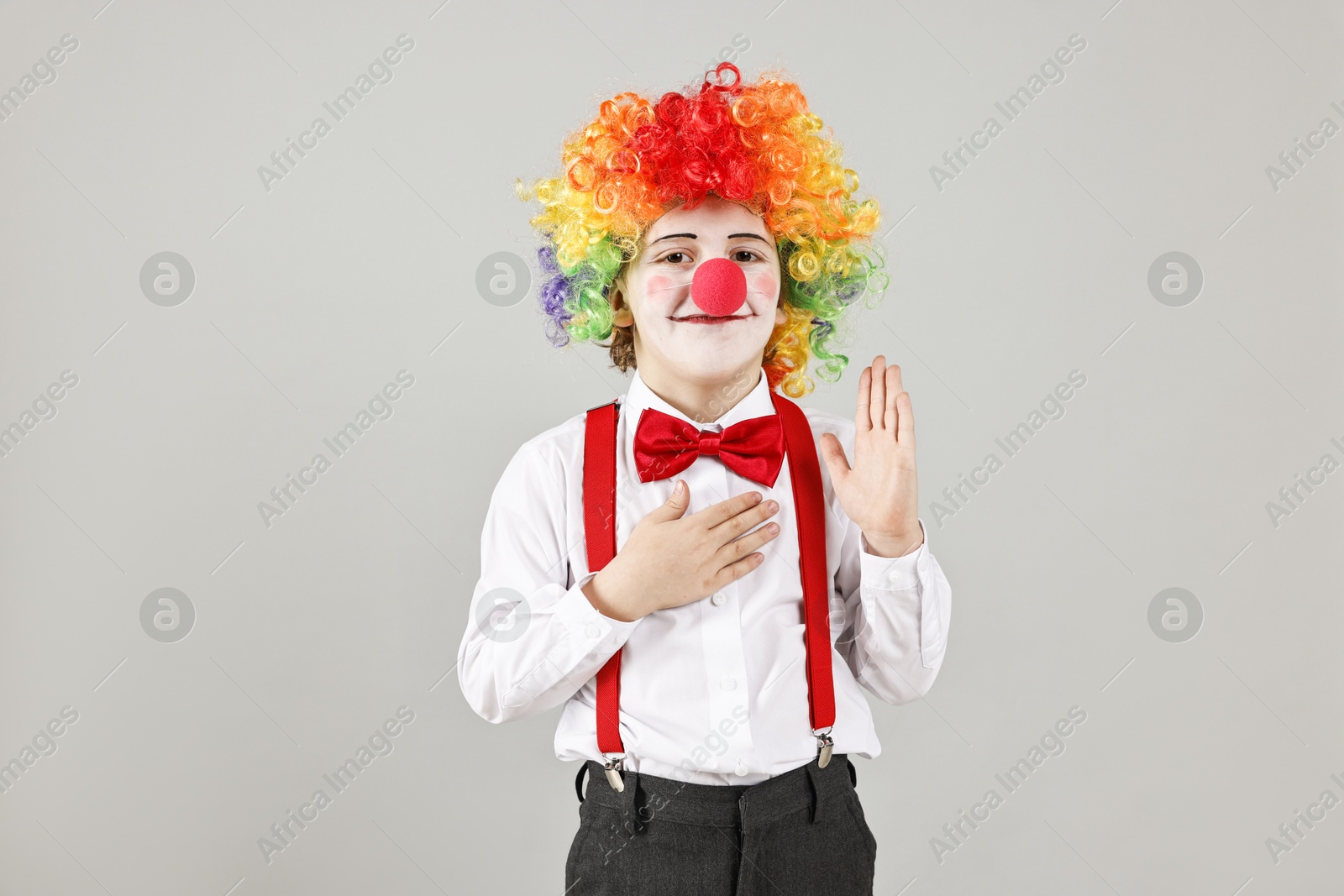 Photo of Cute little boy in clown wig and red nose on grey background. Surprise party