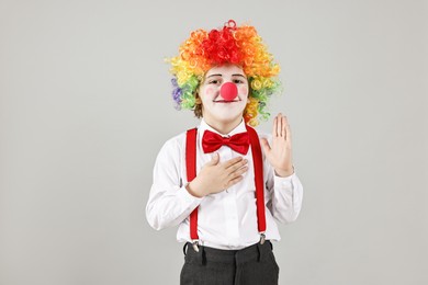 Cute little boy in clown wig and red nose on grey background. Surprise party