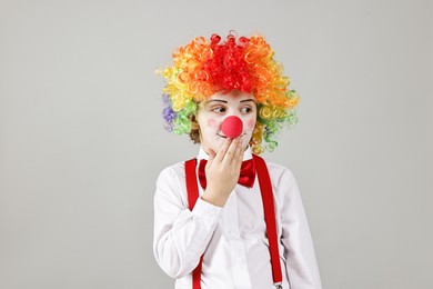 Photo of Cute little boy in clown wig and red nose on grey background. Surprise party