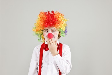 Photo of Cute little boy in clown wig and red nose on grey background. Surprise party